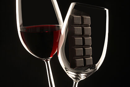 Zwei Weingläser, eines gefüllt mit Rotwein, das andere mit einem Block dunkler Schokolade